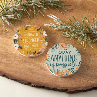 Set of two floral inspirational ceramic car coasters shown in packaging and placed inside standard vehicle cup holders.