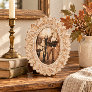 Whitewashed wood oval 4x6 photo frame with carved autumn leaves styled on a warm wood console with vintage books, brass candlestick, and fall foliage.