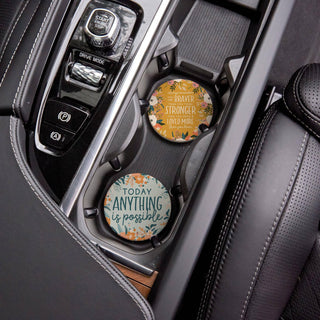 Floral “Braver, Stronger & Loved” and “Today Anything Is Possible” ceramic coasters displayed in a vehicle’s cup holders.