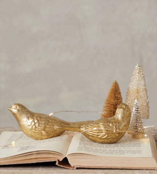 Antique gold cast iron bird figurines styled on an open vintage book with miniature Christmas trees and warm lights