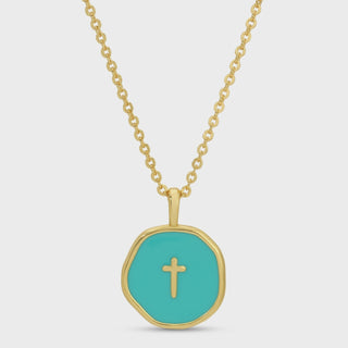 A gold chain necklace with an irregular octagonal pendant featuring a turquoise enamel center and a small gold cross, shown on a light gray background.