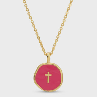 A gold chain necklace with a round, irregular gold pendant featuring a vibrant pink center and a small gold cross in the middle, set against a light gray background.