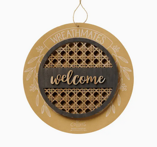 A round hanging decorative sign with a tan wood base, a dark wood center band reading "welcome" in script, woven cane panels behind it, and white line art with the words "WREATHMATES" and "Collins" on a white background.