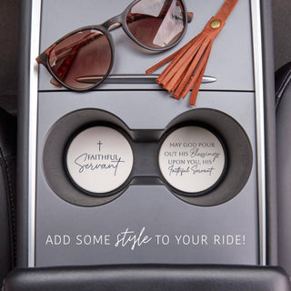 Two Faithful Servant Christian ceramic coasters displayed inside vehicle cup holders beside sunglasses and a leather tassel.