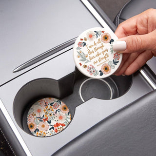 Hand removing the Philippians 4:13 floral car coaster while the coordinating garden-patterned coaster remains in the adjacent cup holder.