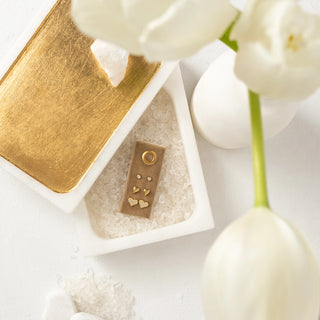Gold necklace with heart details in a white box, surrounded by white flowers.