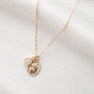 Gold necklace with a pendant and round charm on a white background
