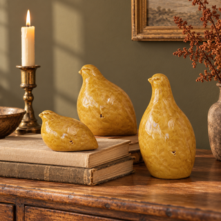 Set of three mustard glazed terracotta quail figurines styled with vintage books and aged-brass accents on a warm wood console.