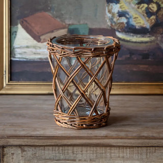 Wicker candle holder on a wooden surface with a painting in the background