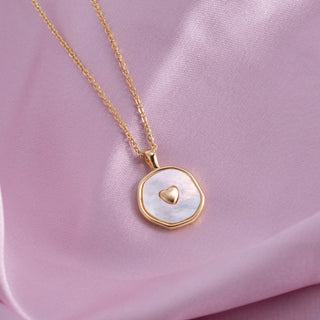 Gold necklace with a heart-shaped pendant on a pink fabric background