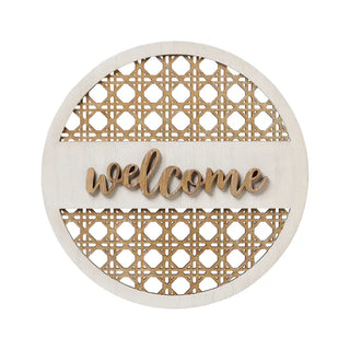 Round wooden wall decor sign with a natural light wood frame, laser-cut geometric cane-style panels in the top and bottom sections, and the word 'welcome' in cursive script across the center.