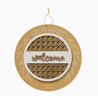 A round hanging wooden sign with a natural wood top loop, featuring a white center band with the word 'welcome' in raised script, and two geometric cane-style panels behind it. The outer ring is tan wood with white line art and the words 'WREATHMATES' at the top; 'collins' appears at the bottom.