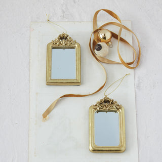 Two gold decorative mirrors with ribbons on a light gray background
