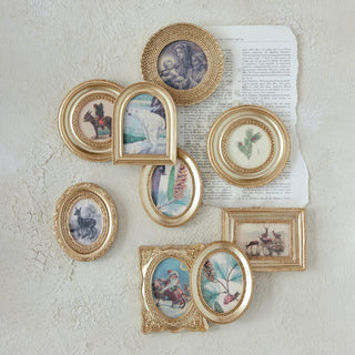 Collection of gold picture frames with various small artworks on a textured wall.