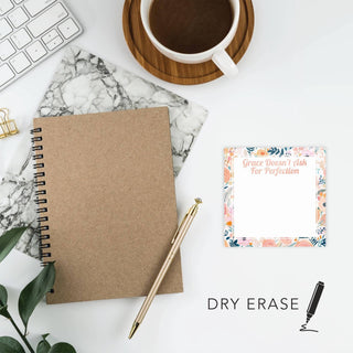 Floral dry erase note tile styled beside a notebook, coffee cup, keyboard, and pen on a home-office desk.