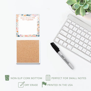 Front and cork-backed views of the floral dry erase tile beside its marker, keyboard, and succulent.